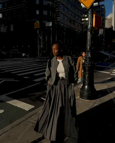 @iamnkirote wears an elegant winter outfit featuring a grey pleated maxi skirt, white top and a cropped wool jacket