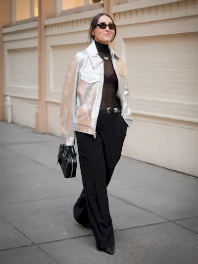 a woman wearing a cute bra under sheer black shirt with a silver jacker and trousers