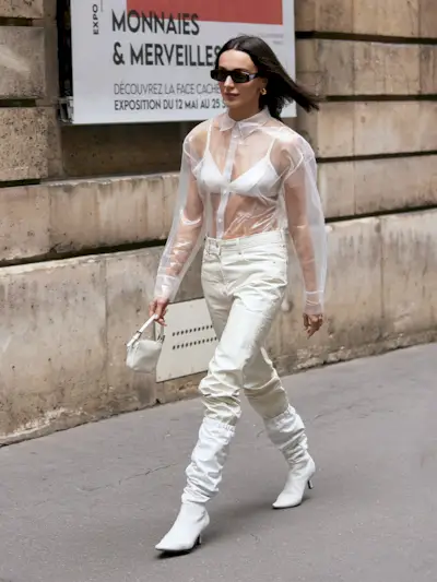 a photo of a woman wearing a sheer white button-down shirt with a white bra with white pants
