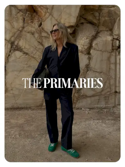 Lucy Williams at the COS S/S 25 show in Greece wearing a navy blue suit and green sneakers. Text reads, 'The Primaries.