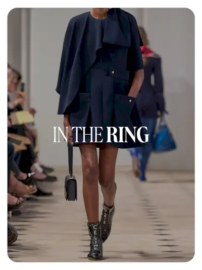 A Celine model walking in a runway show wearing a short coat with high-top black leather boxing sneakers that say Celine on them in white letters. Text reads, 'In the Ring.