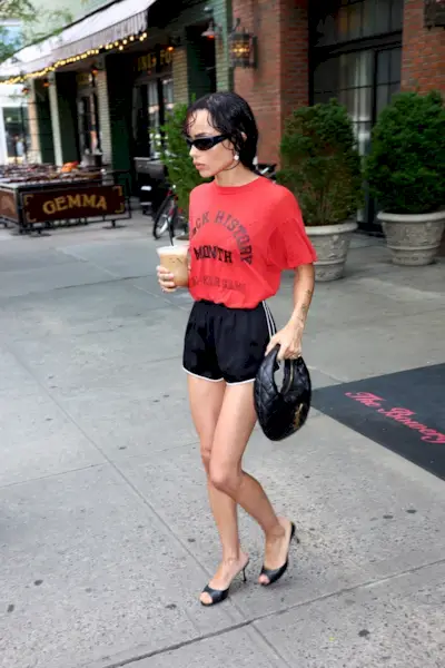 Zoe Kravitz wearing a red t-shirt with black athletic shorts and black kitten heels.