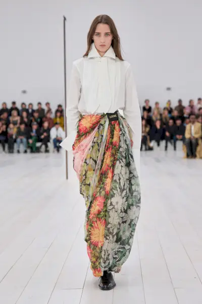 A model wearing a white shirt and floral genie pants on the runway at Loewe