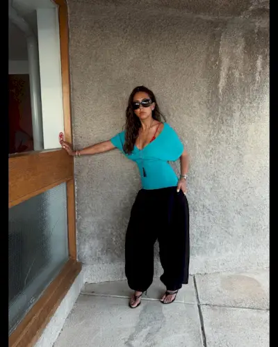 Hanna MW wearing a turquoise off-the-shoulder top with black genie pants and sandals.