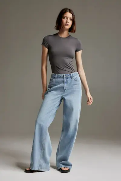 a model wears a gray T-shirt with baggy blue jeans