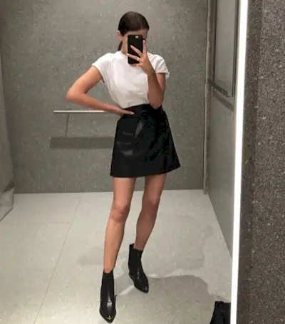 a woman wears a white crewneck T-shirt with a black miniskirt and black ankle boots