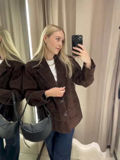 Woman in mirror wears brown suede jacket, White T-shirt and blue jeans