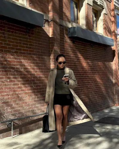 Dawn wears a trench coat, knit jumper, mini skirt and kitten heels