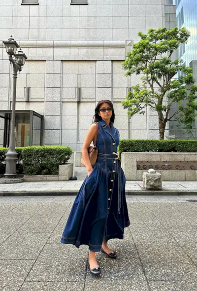 A woman's jean dress outfit with a maxi dress styled with a brown shoulder bag and navy ballet flats.