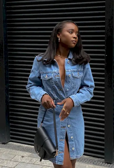 A woman's jean dress outfit with minidress styled with gold jewelry and black Dior Saddle bag.
