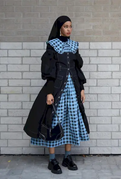 A woman's jean dress outfit with a puff-sleeve denim midi styled over a gingham-print dress with black loafers and blue socks.