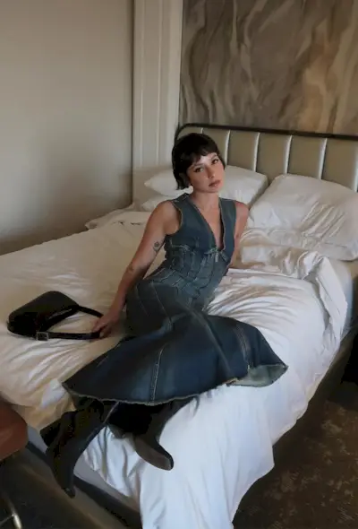 A woman's jean dress outfit with midi dress styled with black ankle boots and black shoulder bag.