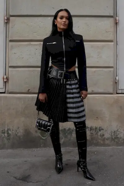 a photo showing what to wear to a rap concert with a woman wearing a cropped jacket with a plaid midi skirt and knee-high boots and a black shoulder bag