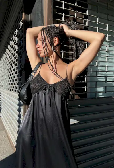 a photo showing what to wear to a rap concert with a woman wearing large hoop earrings with a black slip dress and black crescent bag