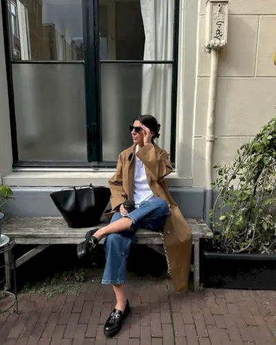 Woman wears trench coat, white shirt, blue jeans and loafers