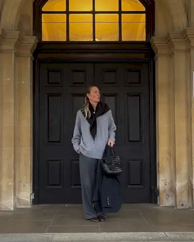 Woman wears knit scarf, grey jumper, grey trousers