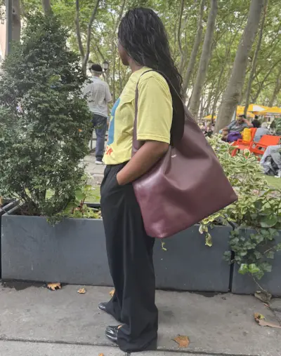 A woman wearing a yellow shirt, black pants, and a burgundy Brooklyn Shoulder Bag