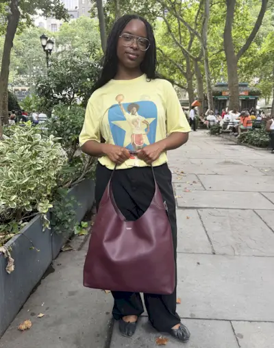 A woman wearing a yellow T-shirt, black pants, and a Coach burgundy Brooklyn Shoulder Bag