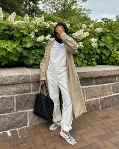 Yusra Siddiqui wearing overalls and Vans checkered sneakers and beige trench coat