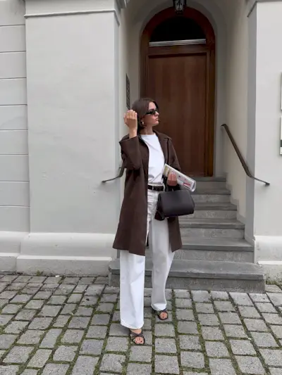 Influencer @maryljean wears white jeans with brown heels, a white-shirt and a brown knee-length jacket.