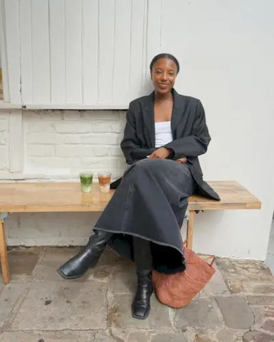 Woman wears black blazer, white top, denim skirt and boots