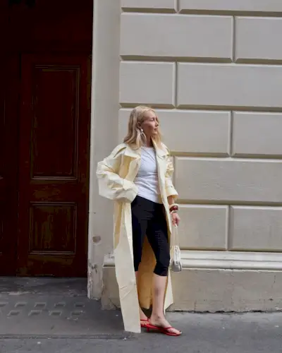 Woman wears yellow trench coat, white T-shirt, black capri pants and red sandals