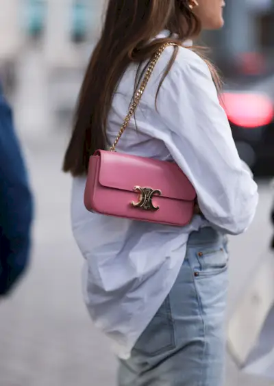 A woman wearing the Celine Triomphe bag in pink with a button-down shirt and light-wash jeans.