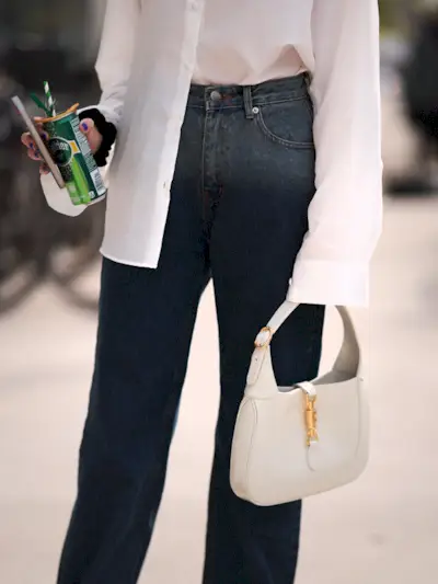 a photo of a woman carrying a designer Gucci Jackie handbag in white with blue jeans, and a white button-down shirt.