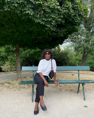 A woman wears a white t-shirt, black capri pants, black heels, and a black shoulder bag.
