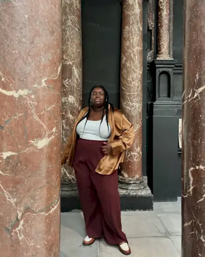 Abi wears a satin jacket, white tank top, burgundy pants, and white loafers.