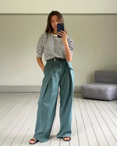 A woman wears a black and white stripe long-sleeve shirt, wide-leg pants, a black belt, and black flats.