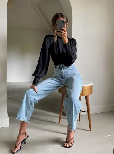 A woman wearing a black blouse, straight-leg jeans, and black heels.