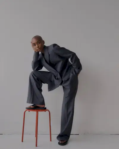 A woman wearing a gray pants suit with black flip-flops.
