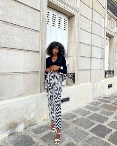 Andi wearing printed pants, a long-sleeve crop top, and white heels.