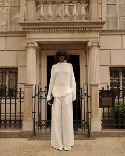 Amy wearing white trousers, a sheer sweater, and a clutch.