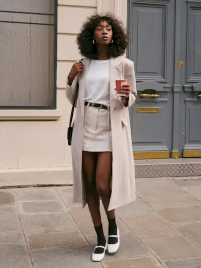 a photo of a long coat with a white T-shirt, belt, miniskirt, socks, and ballet flats