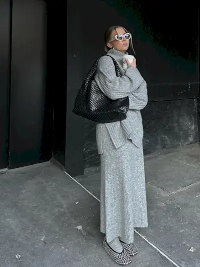 a photo of an influencer wearing a gray turtleneck top with a matching maxi skirt and socks with rhinestone ballet flats and a woven shoulder bag