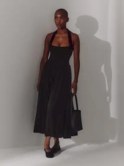 a photo of a woman wearing a black halter dress with a matching shoulder bag and Mary Jane flats