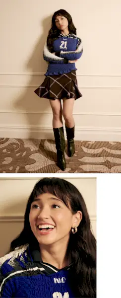 Overcompensating actress Wally Baram poses for portrait at the Plaza Hotel in NYC. She is wearing a long-sleeve smocked blue shirt with the number 21 on the front and a purple plaid miniskirt with black leather boots that hit just below the knee.