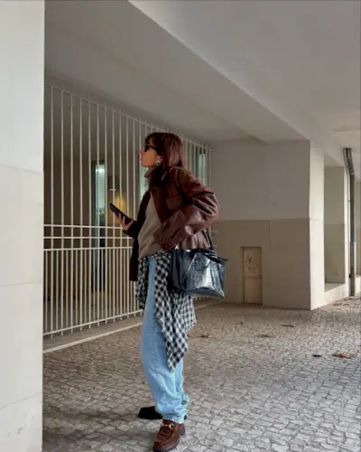 Fashion influencer @emilie_tla wearing a burgundy leather jacket, faded blue jeans, and trendy suede loafers..