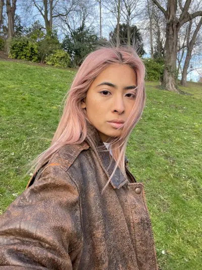 Fashion influencer @himichelleli with pink hair wearing a distressed brown leather jacket.