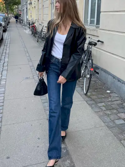 Fashion influencer @claradyrhauge on the street wearing. a black leather blazer, blue jeans, white tank, and sling-back pumps.