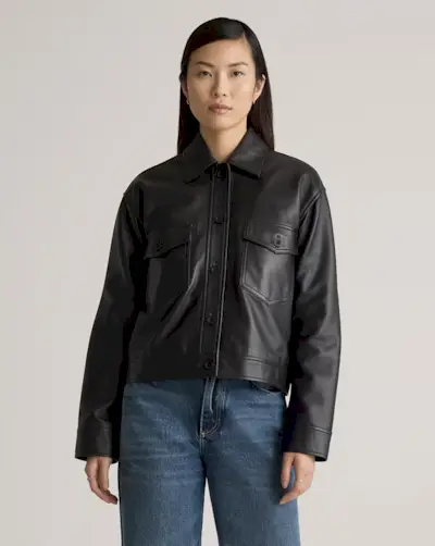 Fashion influencer @aude_julie on the street wearing a vintage-look, collared, black leather jacket with a turtleneck, blue faded jeans, burgundy heels, a Louis Vuitton handbag, and cap.