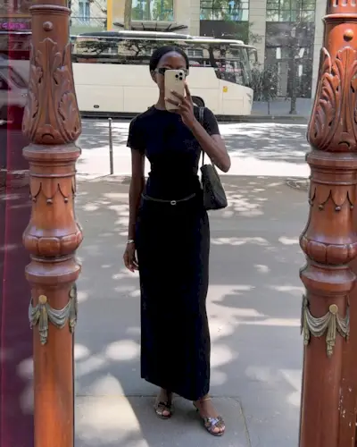 @sylviemus_ wearing a black T-shirt dress and heeled sandals.
