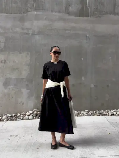 @dawn.tan wearing a black T-shirt dress with a white sweater around waist and ballet flats.
