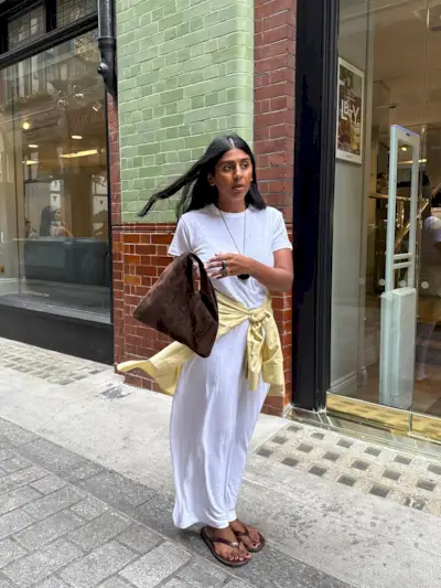 @monikh wearing a white T-shirt dress with a yellow shirt around her waist with flip-flops.