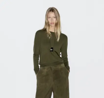 @monikh wears black trousers, green jumper and black flip flops