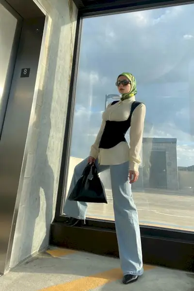 a woman's corset top outfit with a black underbust corset styled over a white button-down shirt styled with wide-leg jeans and pointed heels