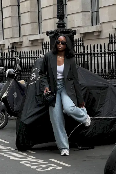 a photo showing what shoes to wear with bootcut jeans, specifically a woman wearing a black blazer over a white tank top with light wash bootcut jeans and chunky white sneakers