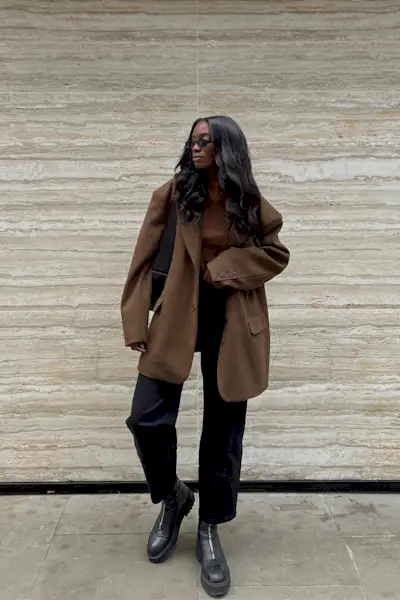 a photo showing what shoes to wear with bootcut jeans, specifically a woman wearing an oversized brown blazer over a brown t-shirt with black bootcut jeans and black chelsea ankle boots